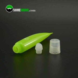 A green small size cosmetic tube lipstick tube with offset printing and small PP cap, with its cap removed, lying next to a transparent cap and a white applicator tip on a reflective surface.