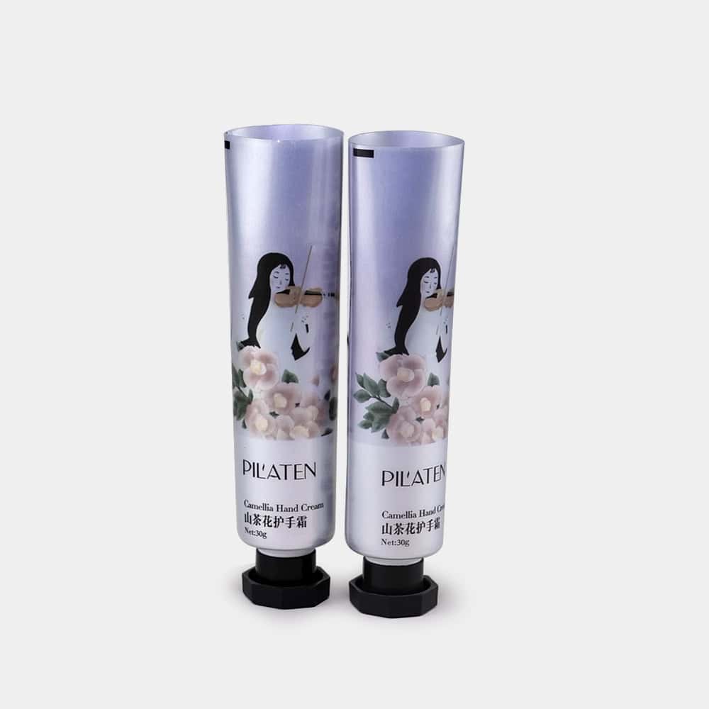 Dua tiub Pil'aten Camellia Hand Cream, dihiasi dengan reka bentuk bunga dan biola, mempamerkan estetika tiub berlamina moden.