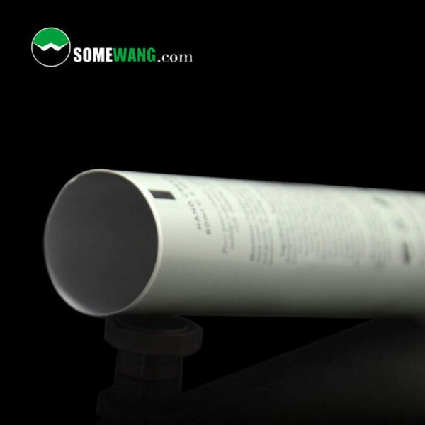 Phrase avec le nom du produit : Gros plan d'un tube laminé en plastique d'aluminium souple de 80 ml à 100 ml avec un capuchon en anis noir, portant le texte « somewang.com » sur un fond sombre.