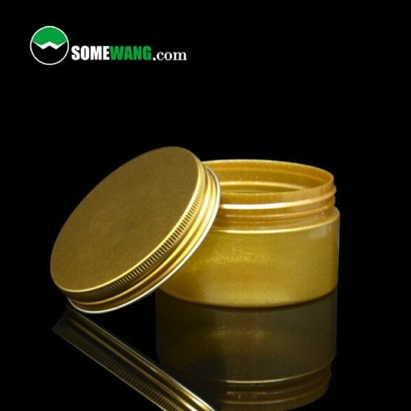 Sentence with product name: An open golden cosmetic jar with a reflective lid lying beside it, placed on a dark glossy surface with the brand "somewang.com" logo visible in the corner, available as 89mm jars wholesale | 100g - 1000g | 92mm Diameter | Customization Options