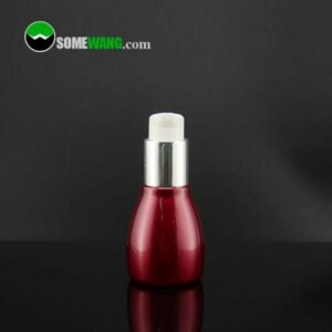 Koyu arka planda yansıtıcı siyah yüzey üzerinde tedavi pompası dağıtıcısı bulunan küçük kırmızı High End PET losyon şişesi.