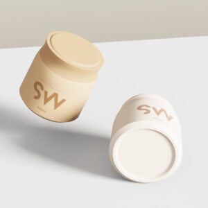 Two beige and off-white SWC-JP300BD jars, one upright and one lying down, on a minimal light background.