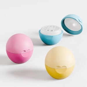 Drei pastellfarbene, eiförmige Silikonbehälter in Rosa, Gelb und Blau. Einer ist offen und zeigt ein gitterartiges Inneres. Jeder Behälter fasst 7 g Mini-Lippenbalsam.