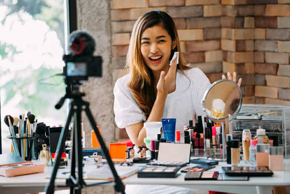 Encantadora chica asiática grabando vlog. Blogger de belleza que presenta cosméticos de maquillaje frente a la cámara