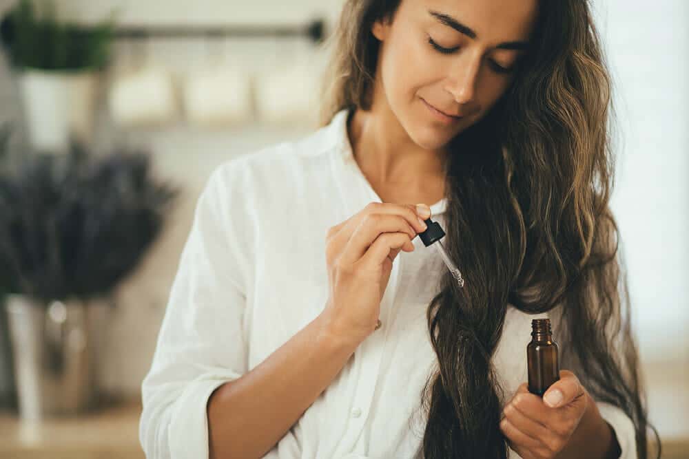 Young woman applying natural organic essential oil on hair and skin