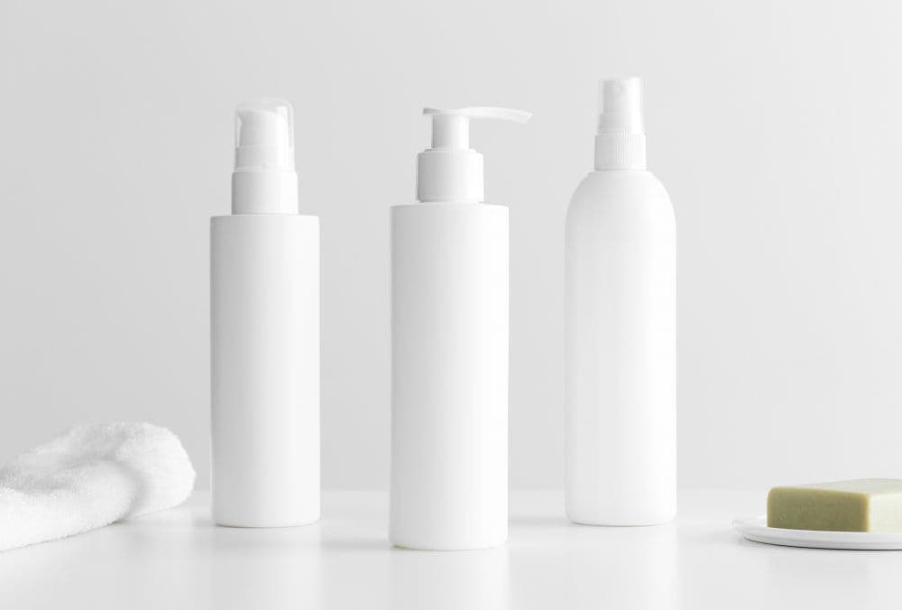 Set aus weißen Kosmetikflaschen mit einem Handtuch und einer Naturseife auf einem weißen Tisch