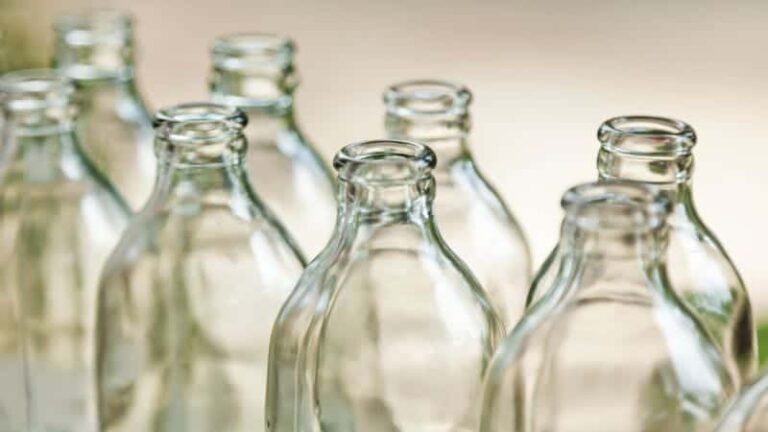 تُظهر الصورة المُرفقة مجموعة من الزجاجات الفارغة مُرتبةً في صف، مع التركيز على لمساتها النهائية. الزجاجات مصنوعة من زجاج شفاف، وتتميز بتصميم قياسي برقبة ضيقة وقاعدة أوسع، وهو ما يميز العديد من زجاجات المشروبات. جميع الزجاجات متماثلة في الحجم والشكل، مما يُشير إلى أنها جزء من مجموعة أو دفعة.