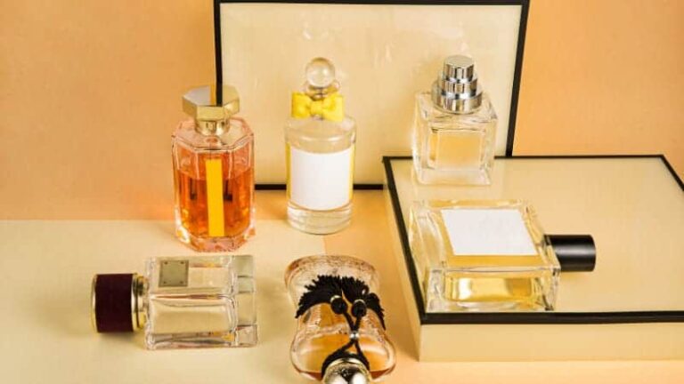 تشكيلة من زجاجات العطور، لكل منها تصميم عبوة زجاجية فريد. الزجاجات مرتبة على سطح مستوٍ على خلفية بلون الخوخ أو البيج، مما يخلق عرضًا أنيقًا وفخمًا.