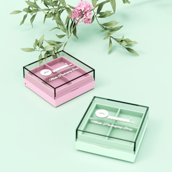 Dos paletas de sombras de ojos de cuatro colores (rosa y verde con tapas transparentes) se encuentran junto a una flor rosa sobre una superficie verde claro.