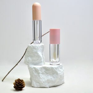 Twee PETG-lipglosstubes van 15 ml, weergegeven op een witte getextureerde steen met een kleine dennenappel en een takje ernaast, tegen een effen lichte achtergrond.