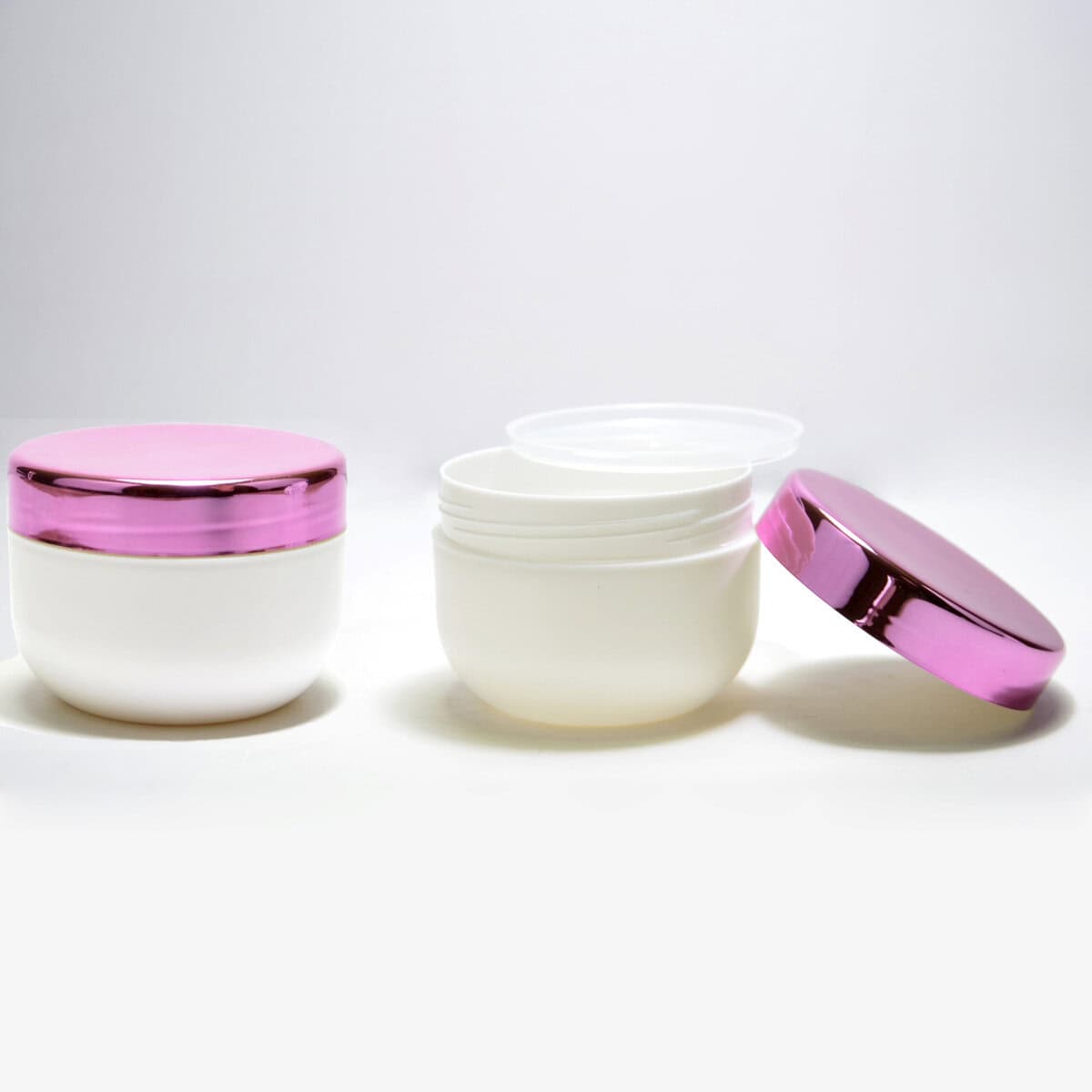 Three 200ml PP Jars for personal care with pink metallic lids on a white background, the middle jar's lid is off showing its contents.