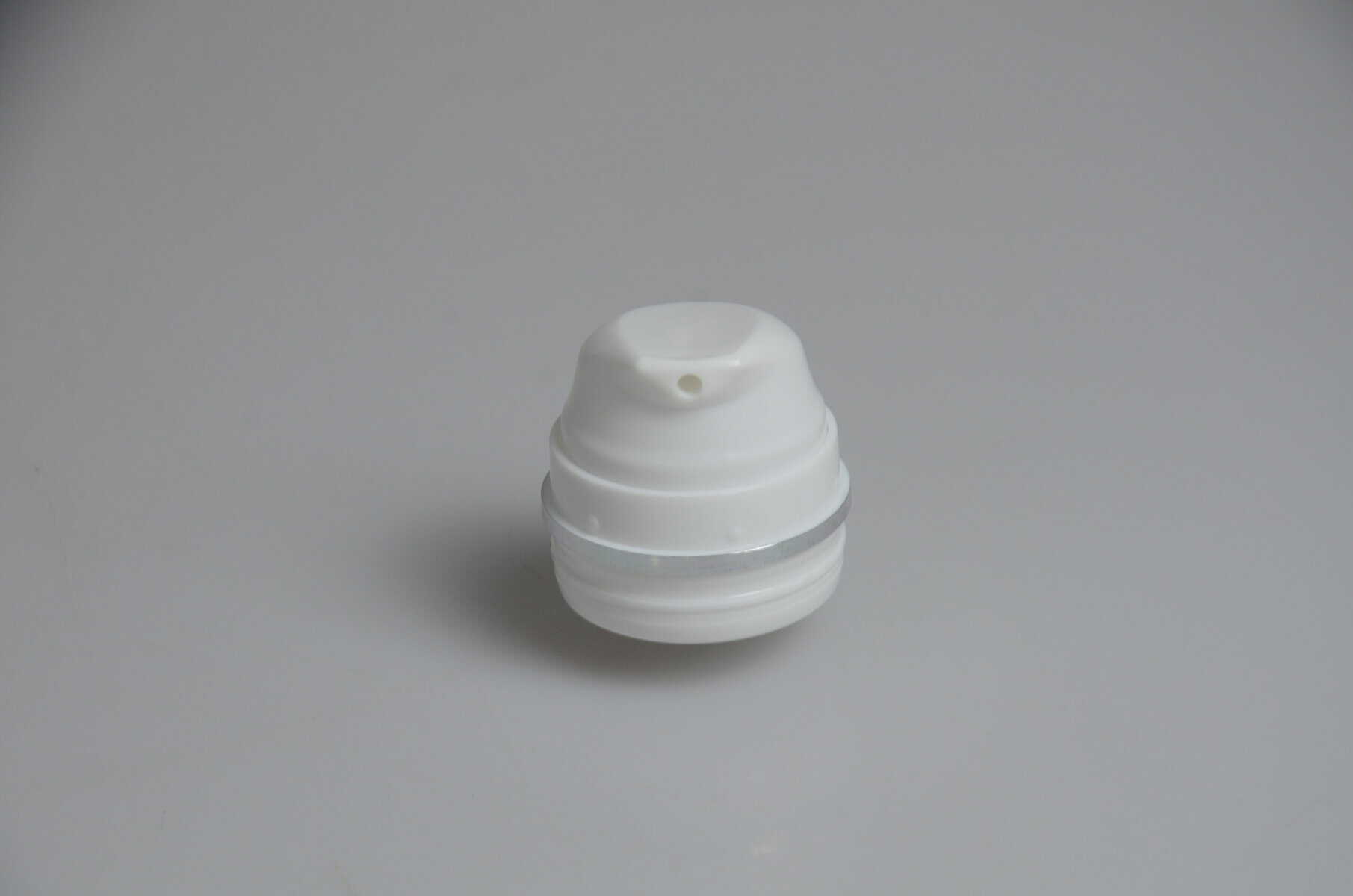 A white plastic cap with a central hole fits snugly on a 30-150ml Airless Bottle Round Output Mouth, placed on a light gray surface.