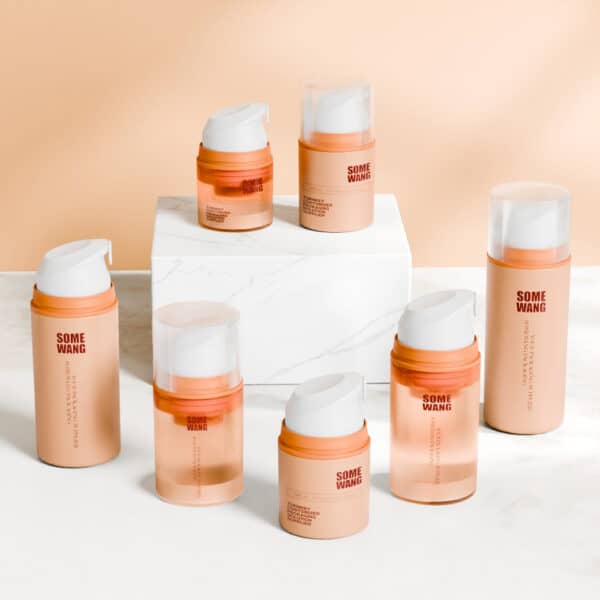 Skincare products in sleek 50ml orange and white airless pump bottles labeled "SWC-BPA20 PP Material," arranged around a white block.