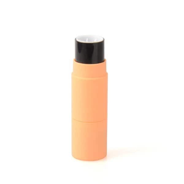 A peach-colored cylindrical container with a black cap, resembling a concealer or lipstick stick, stands upright on a white background.