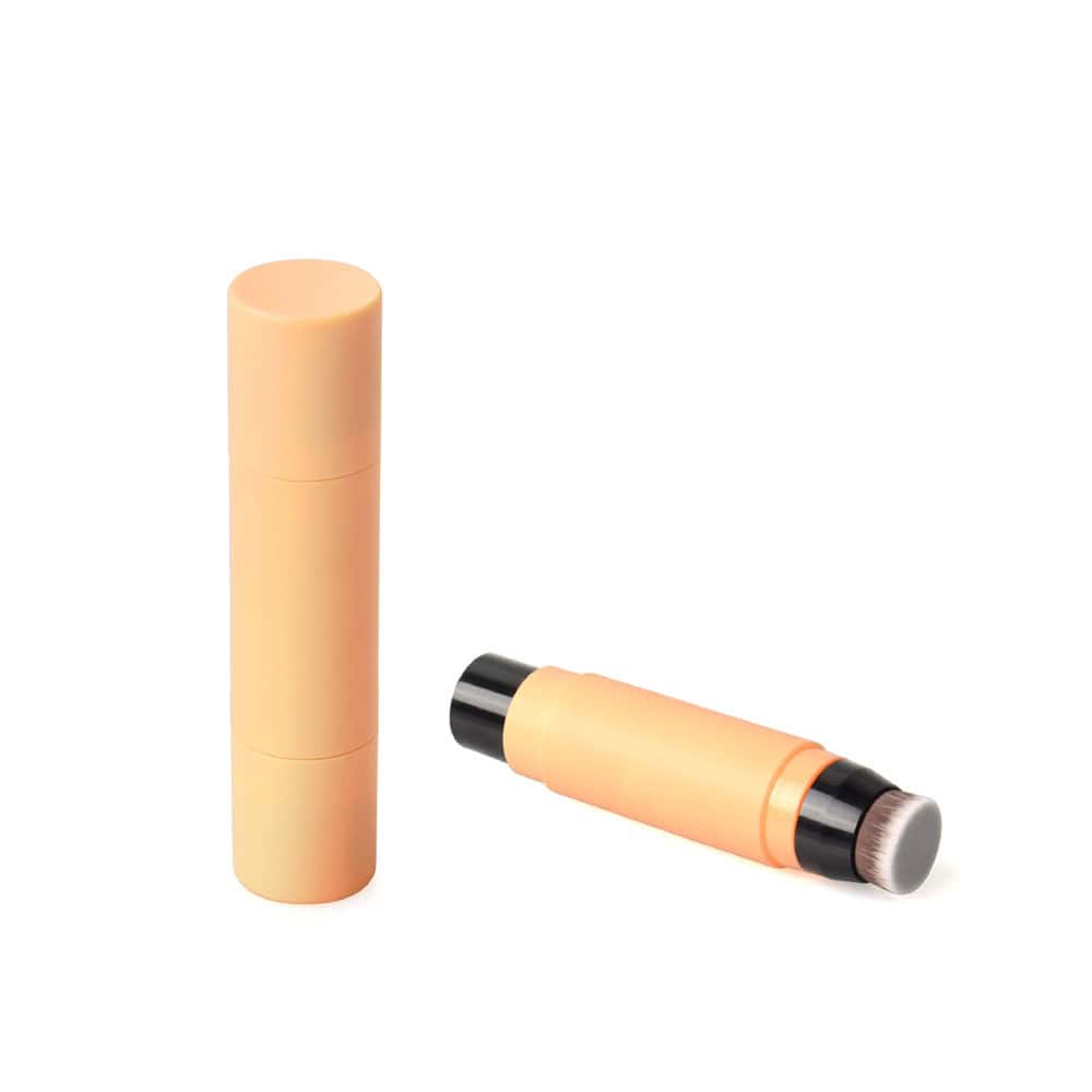 Ein zylindrischer, orangefarbener Concealer-Highlighter-Stick (5 g/8 g), abgebildet mit und ohne Kappe, sodass ein Applikatorpinsel zum Vorschein kommt.