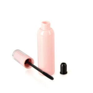 Een roze, open cilindervormige plastic mascaratube met een zwart borsteltje ernaast en een klein zwart dopje aan de rechterkant.