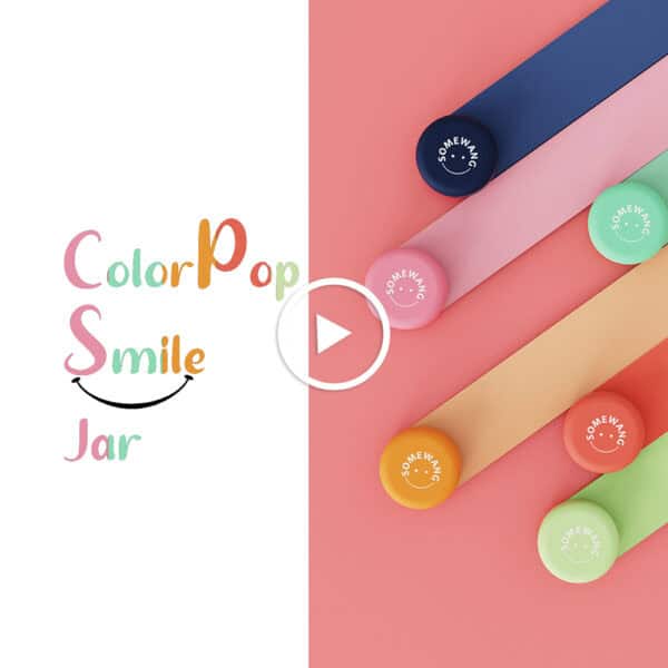 Anuncio de ColorPop Smile Jar: cinco frascos coloridos con tapas en tonos macarrones dispuestos en diagonal sobre una superficie rosa. Botón de reproducción centrado.