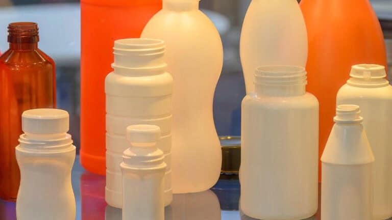 Custom white and orange PET plastic bottles stand upright on a reflective surface.