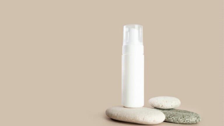 Airless pump bottle on a beige background, balanced on smooth stones, showcasing innovative cosmetic packaging.