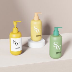 Drie 300ml PE SW-geëtiketteerde pompflacons (geel, beige op platform, groen) voor toiletartikelen op een licht houten oppervlak.
