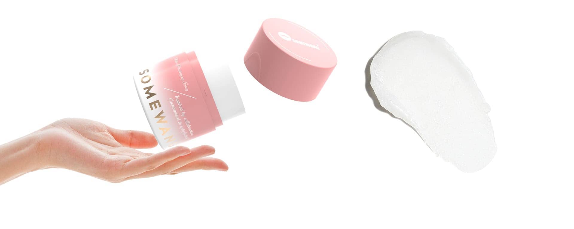 A hand tosses an open pink "Somewan" cream jar beside a white balm smear on a white background.