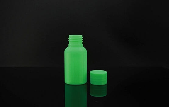 A small green plastic bottle with its matching cap beside it on a black background.