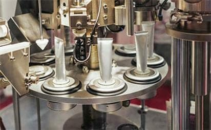 A tube filling and sealing machine fills upright tubes on a rotating circular platform.