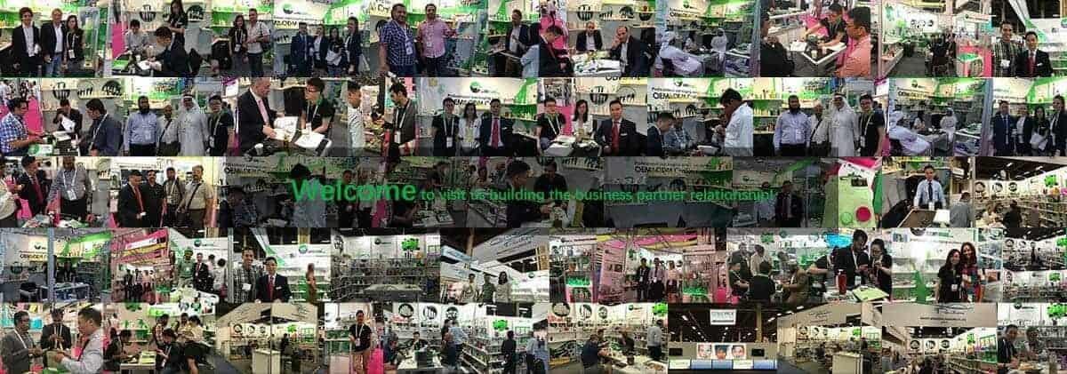 Businesspeople networking and presenting products at a trade show with green-themed company booths in the background.