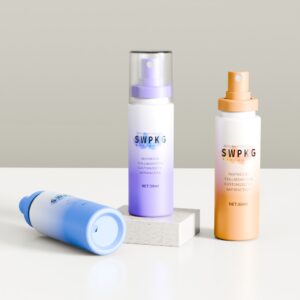 Drie 50/60 ml blauwe, paarse en oranje PET-flessen met opklikbare verstuivers - twee staand en één liggend.