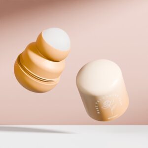 Kayu dan penutup kosmetik kuning air, digayakan seperti botol roll-on 50ml, terapung pada merah jambu dengan grafik mawar dan teks anggun.