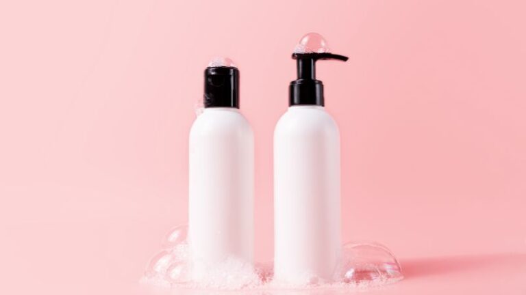 زجاجتان أبيضتان للعناية بالبشرة بأغطية سوداء ومضخة توزيع على خلفية وردية ناعمة، تعرضان عبوات منتجات تجميل بسيطة للعناية بالبشرة ومستحضرات التجميل.